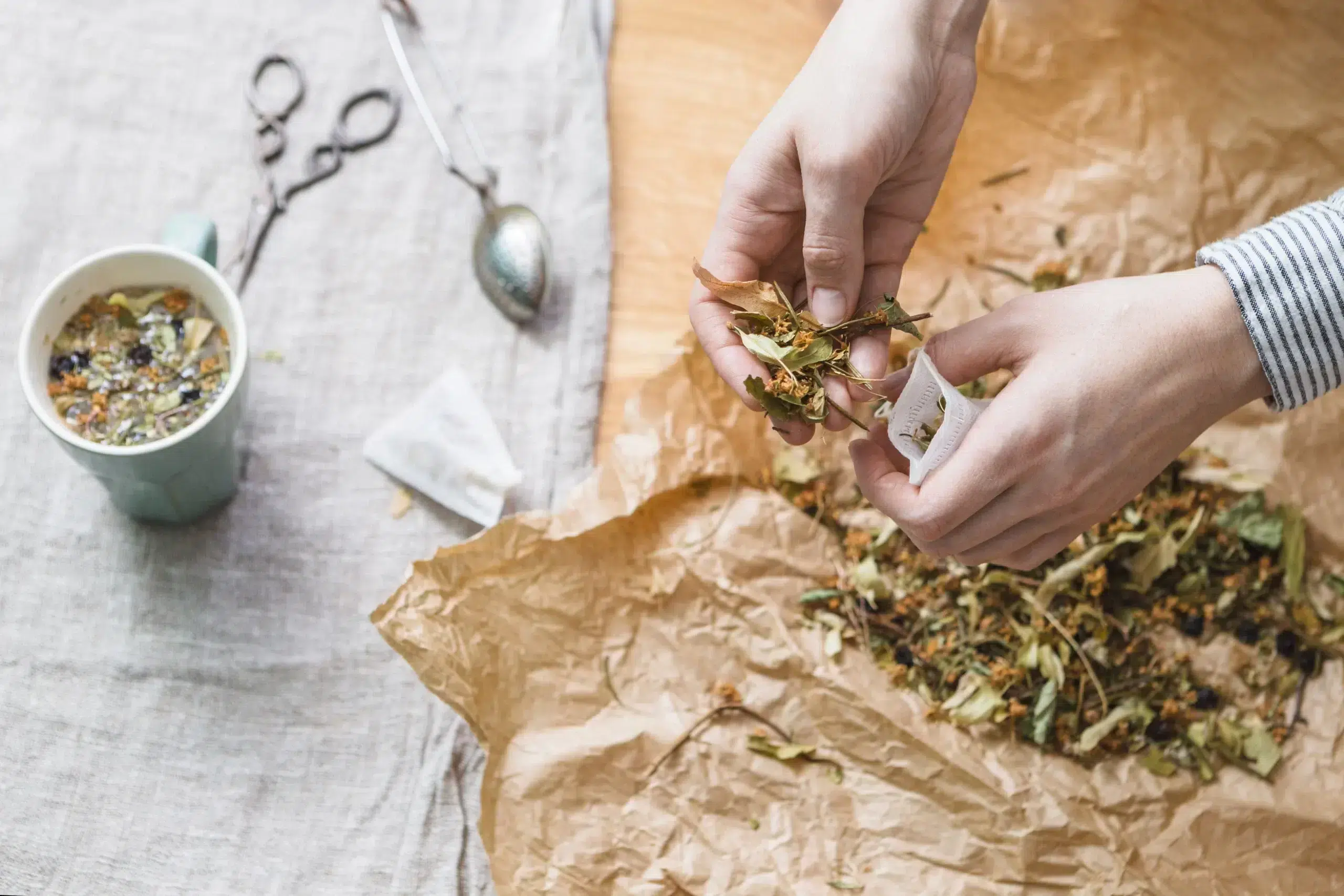 Hands putting herbal mixture into tea bag scaled